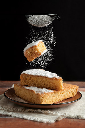 Delicious freshly baked sponge cake whit piece of cake falling and sprinkling icing sugar