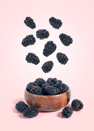 Ripe blackberries falling into a wooden bowl