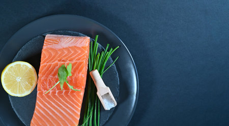 Fresh raw salmon fish fillet, herbs and lemon on black background with copy space, top view