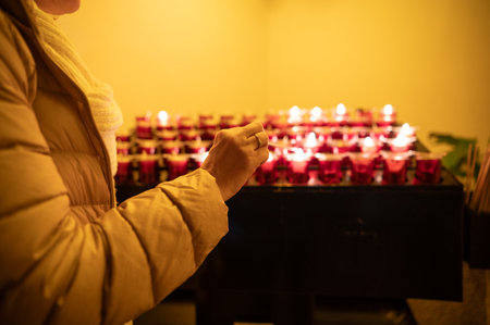 Woman lighting a red candle in a church, making a wish, hope or prayerの写真素材