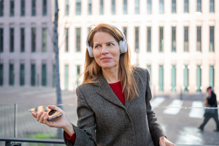Smiling businesswoman listening to music using headphones and smartphone in urban city contextの写真素材