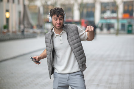 Carefree young man enjoying music through his headphones, holding his phone and dancing on a city streetの写真素材