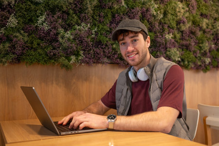 Smiling man using a laptop in a cafe with a green wall