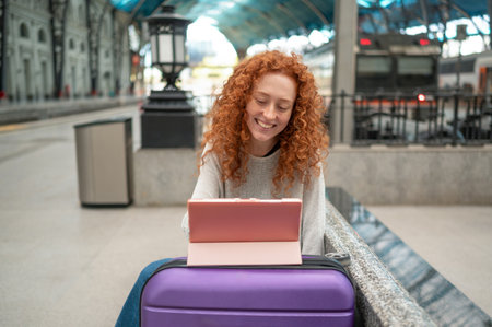 Smiling young woman using tablet while waiting for train at stationの写真素材