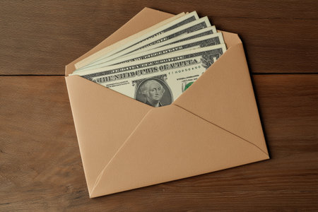 Envelope containing several one dollar bills on a wooden table, suggesting themes of finance, savings, and money managementの素材