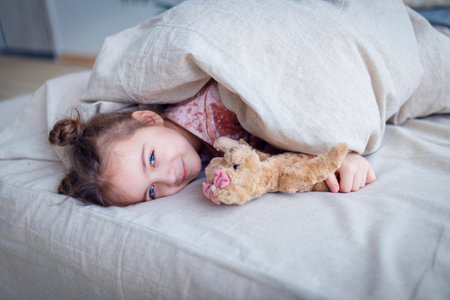 Pretty little girl with a bear teddy lies in bedの写真素材