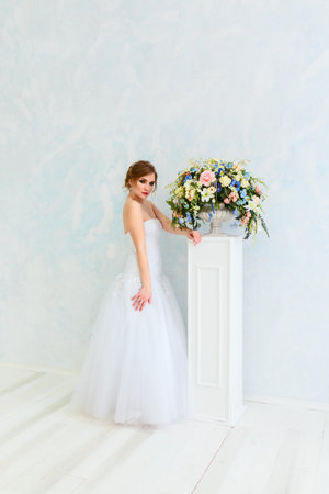 Bride in beautiful dress sitting on chair indoors in white studio interior like at home. Trendy wedding style shot. Young attractive multi-racial Asian Caucasian model like a bride tender looking.の写真素材