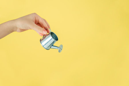 hand holding a small watering can, on a yellow background with a copy of the spaceの写真素材
