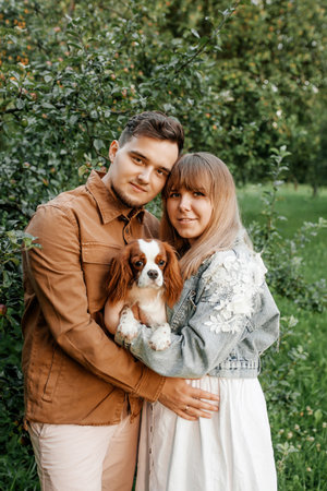 young happy couple standing near trees in the park and holding a dogの写真素材