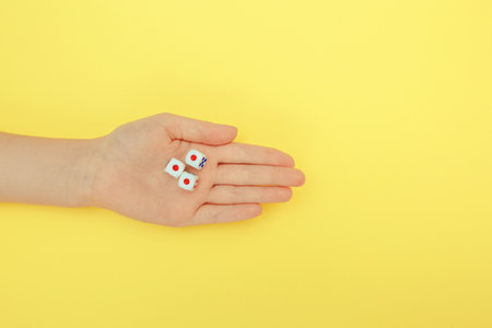 A woman's hand holds three dice. A game of dice with numbers. Board game items. yellow background.の写真素材