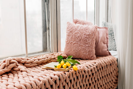 Pillows and a knitted blanket, a book and flowers on the windowsill. Cozy winter window sill.の写真素材