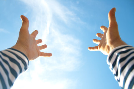 Hands raised up in air across blue skyの写真素材
