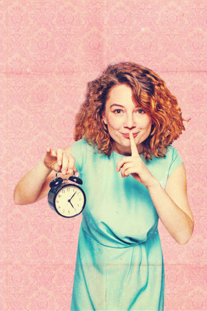 beautiful young woman with alarm clock in studioの写真素材