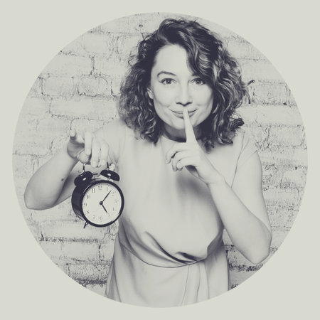 beautiful young woman with alarm clock in studioの写真素材