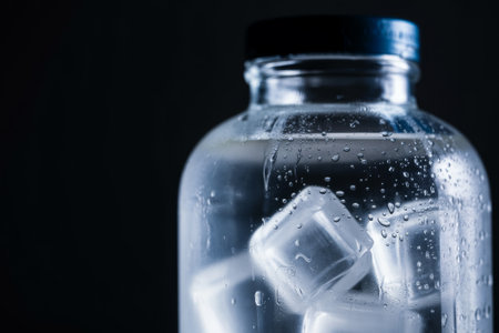Close up view of a glass jar containing clear ice cubes and cold water. The droplets on the jar's surface enhance the refreshing feel, perfect for a hot day or a thirst quencher.の素材