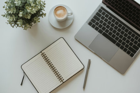 A clean desk setup showcases a laptop, an open notepad with blank pages, a cup of coffee, and a small green plant, creating an inspiring work environment.の素材