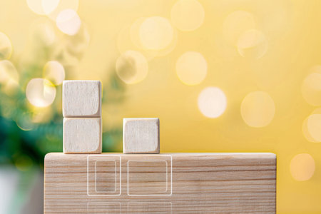 Wooden blocks stacked on a weathered wood table against a blurred background of green leaves and a bright yellow wallの素材