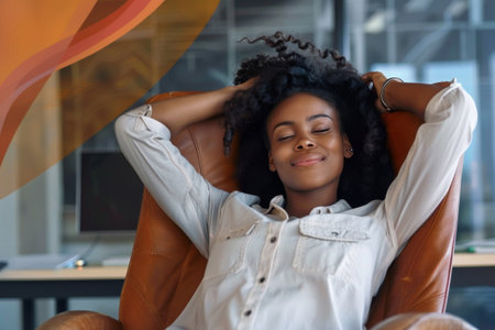 A young professional woman leans back in her office chair, enjoying a moment of calm and relaxation with eyes closed.の素材