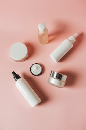 Various skincare bottles and cosmetic jars are arranged attractively on a soft pink background. This setup highlights a beauty routine and elegant product design, inviting interest in skincare.の素材