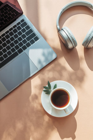 A laptop rests on a light surface next to a cup of coffee and headphones. Sunlight casts soft shadows, creating a warm and inviting atmosphere for productivity.の素材