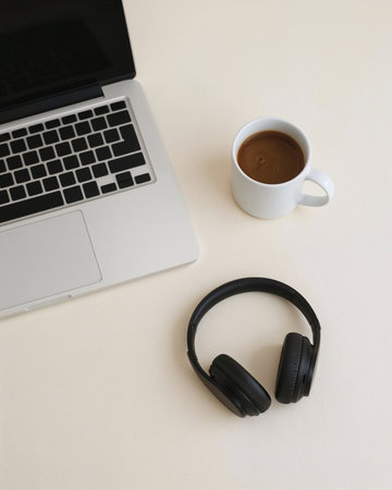A modern laptop rests on a clean desk, paired with a cup of coffee and wireless headphones. The scene captures a cozy and productive workspace, perfect for working or studying.の素材