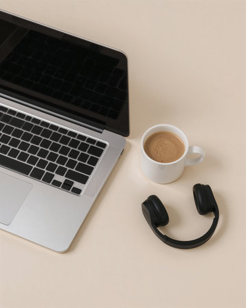A modern laptop rests on a smooth, light surface next to a white coffee cup and black headphones. This setup creates a cozy workspace ideal for productivity or relaxation.の素材
