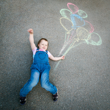 Little Girl with balloons drawing with chalk on the pavementの写真素材