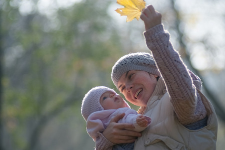 Mom and baby looking at the yellow maple leaf on outdoorsの写真素材