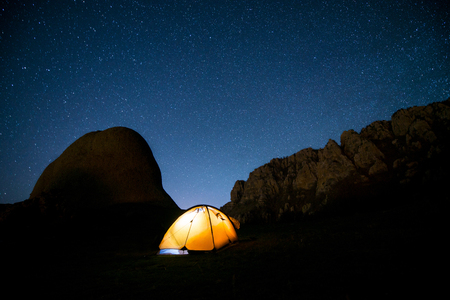 Glowing tent in the mountains under a starry skyの写真素材