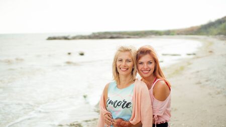 Adult daughter hugs mom on the sea shore and both are smilingの写真素材