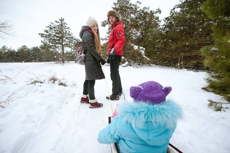 Dad and mom ride a child on a sledge in the winter outdoors. Happy family.の写真素材