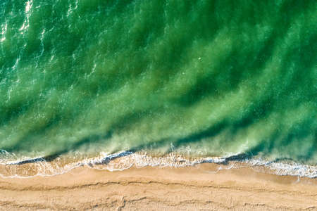 The scenic sea of green color with waves and sandy shore. Aerial view.