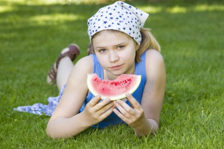 cute little girl eating watermelon on the grassの写真素材