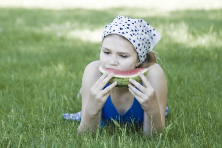 cute little girl eating watermelon on the grass  の写真素材