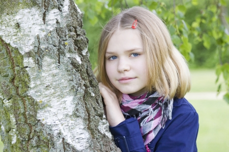 Portrait of young girl standing near birch tree at summer green parkの写真素材