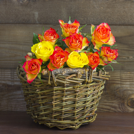 orange and yallow roses in a basket on wooden backgroundの写真素材