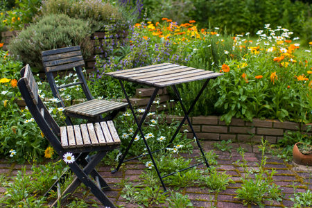 wild garden - herb spiral in the garden with fresh herbs and flowers, table and chair