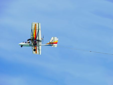 Shot taken from the beach of a colorful ultralight plane flying against blue sky and towing a publicity sign (not shown).の写真素材