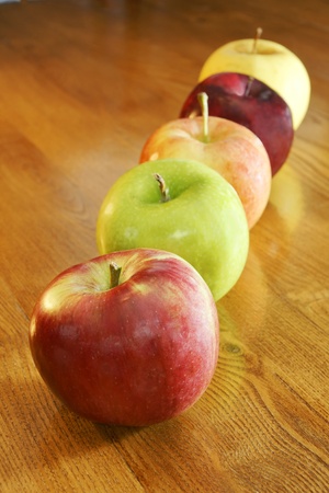Apples of all kinds in a row on a kitchen wooden table: cortland, granny smith, gala, red and golden delicious.の写真素材