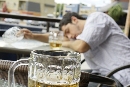 Alcohol abuse: drunk young man or student lying down on a table with beer bock still in hand, focus...