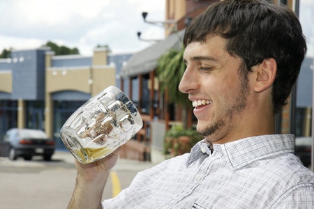 Young man or student happy to find out there is still beer in his glass while sitting outdoor on a bar's terrace during an afternoon on the town.の写真素材