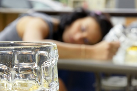 Alcohol abuse: drunk young woman or student lying down on a table with beer bock still in hand, focus on glass up front.の写真素材
