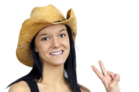 Pretty young cowgirl wearing a straw cowboy hat smiling and making the peace sign with her fingers.の写真素材