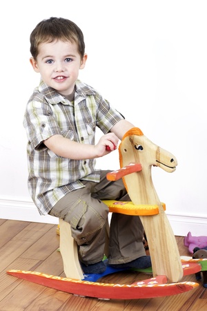 Cute little boy riding a handcarfted wooden rocking horse chair, vertical studio shot.の写真素材