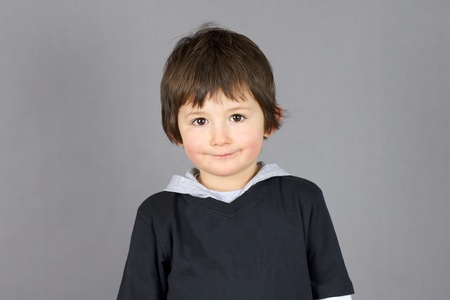 Super cute little boy preschooler with big brown eyes and a charming hint of a smile over grey background.の写真素材
