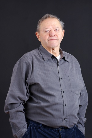 Portrait of an old or senior man smiling from the waist up with hands in his pockets shot in studio over black, great details.の写真素材