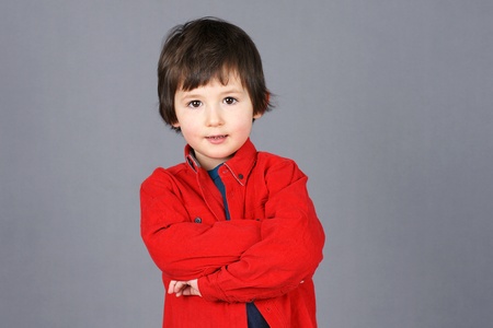 Cute little boy with little smile big brown eyes and crossed arms dressed in red shirt, studio shot over grey background.の写真素材