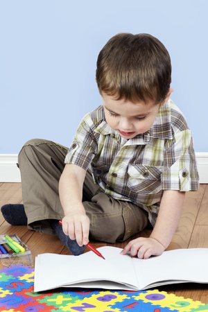 Cute little boy focused while coloring a blank white paper page with a red pen.の写真素材