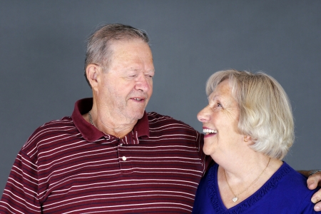 Happy senior couple laughing together, studio shot over grey background.の写真素材