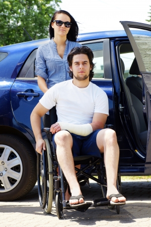 Young couple leaving or arriving to the hospital,young man in wheelchair with a cast on his hand.の写真素材